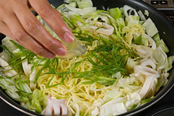 2に焼きそばを入れ、酒を入れてフタをする。少し蒸らしたら、味をみて塩、こしょうを振り、仕上げに白ゴマを振りかける。