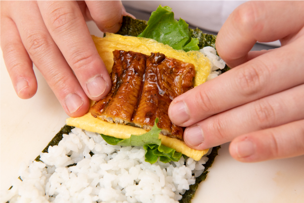 のりにごはん、2の薄焼き卵、うなぎをのせ、お好みで山椒をふり、四角く包んでいく。ラップでくるみ、半分に切って盛り付ける。